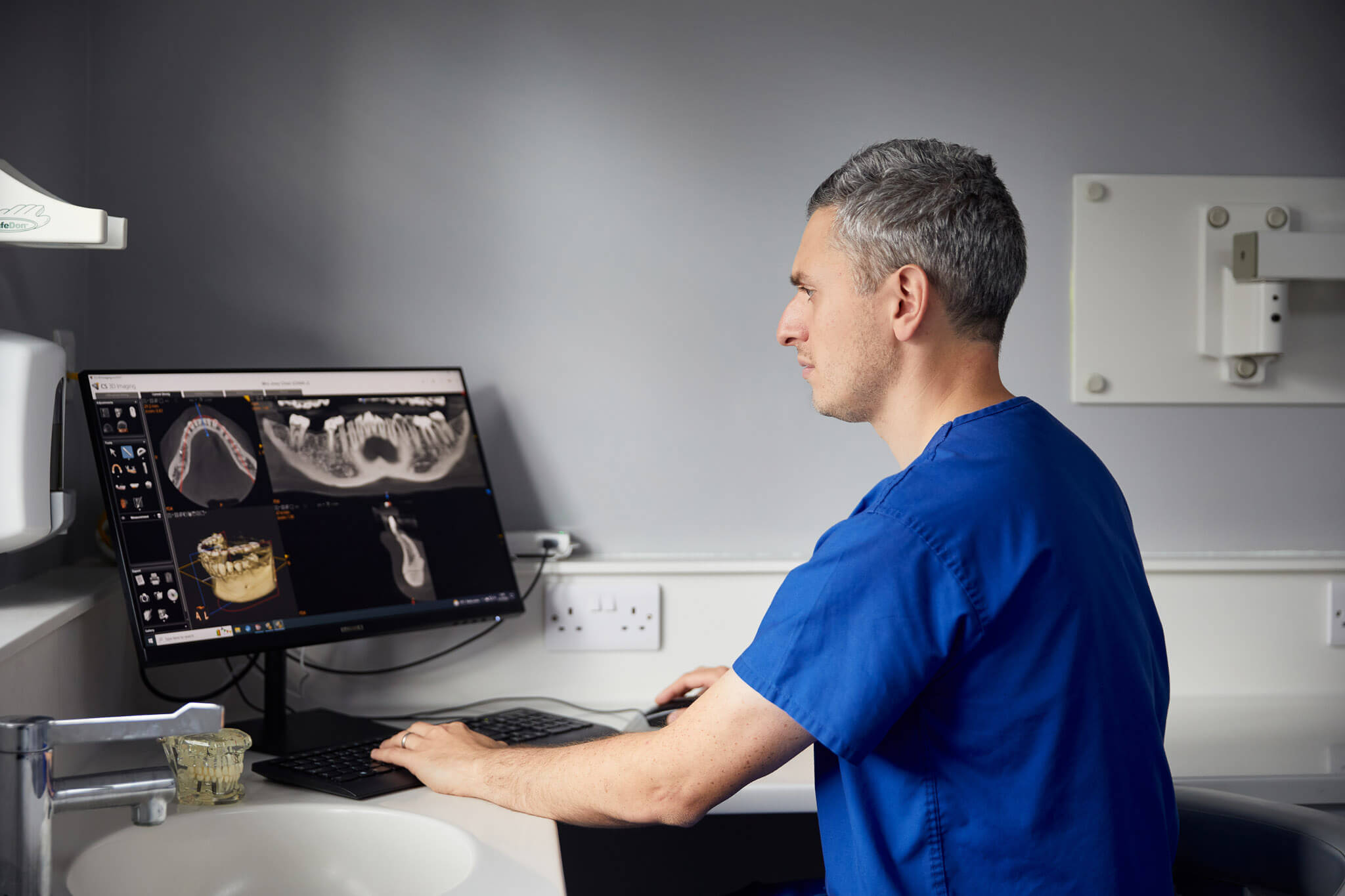 a dentist in blue scrubs looking at X-rays on a computer at our dental practice near Ripon